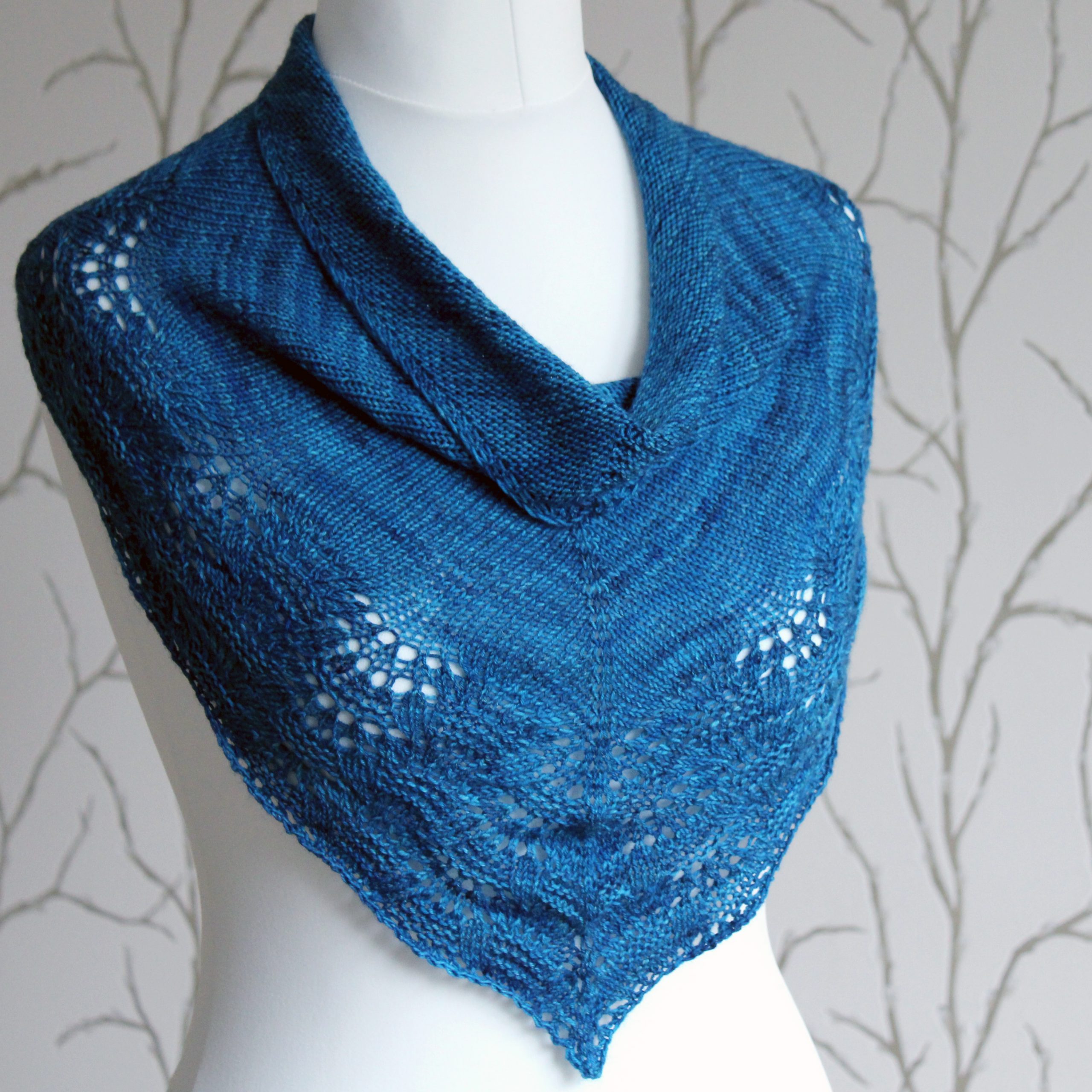 A blue triangular cowlette with a stocking stitch body and rippling lace and textured border