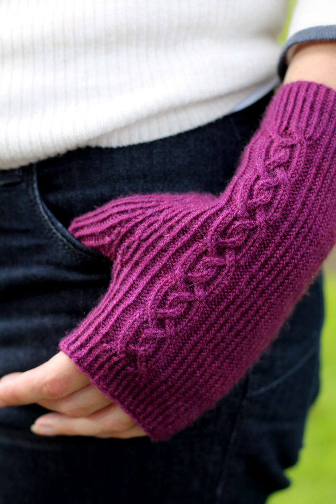 Twisted rib fingerless mitts with a large cable up the back of the hand and a narrow cable pattern that splits around the thumb (thumb tucked into jeans pocket)